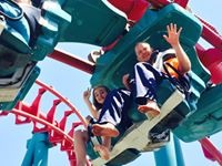 Riders waving on a red and teal roller coaster at Elitch Gardens in Denver, Colorado