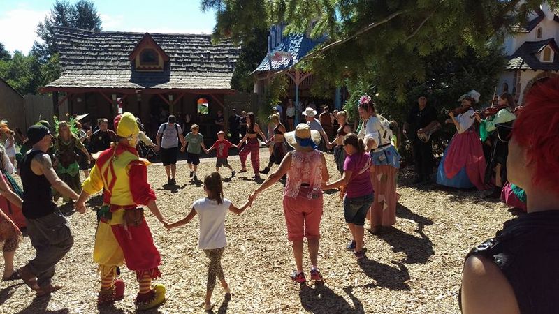 Festival-goers joining a circle dance with a jester at the Colorado Medieval Festival