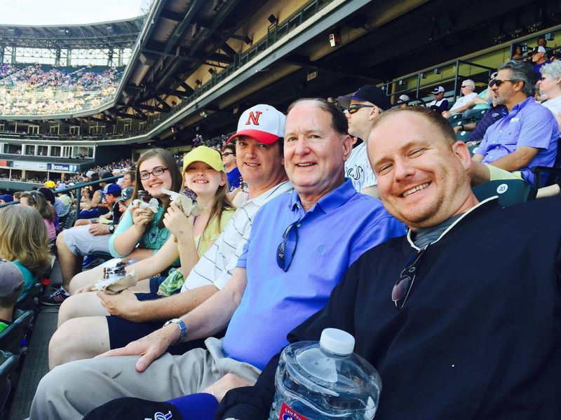 Robert Jenkins smiling with family and friends in the stands at a Colorado Rockies game at Coors Field in Denver